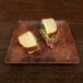 A sandwich cut in half on an Elite Global Solutions checkered bamboo and melamine plate.