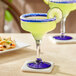 Two Acopa Tropic margarita glasses filled with yellow drinks and lime slices on a table.