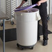 A man putting a scoop into a large white ingredient storage bin with a purple lid.