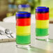 Two Acopa Tropic shooter glasses with multicolored liquid on a table.