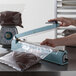 A person using an Omcan manual impulse bag sealer to seal bags of chocolate.