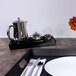 A black rectangular melamine room service tray with silverware and a teapot on it.