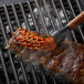 A piece of meat being basted on a grill with an Outset silicone BBQ mop brush.