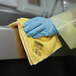 A gloved hand holding a yellow Rubbermaid microfiber cloth.