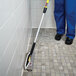 A person in blue scrubs using a Rubbermaid Quick-Connect Flexi-Frame Microfiber Wet / Dry Mop to clean a tile floor.