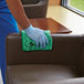 A person cleaning a chair with a green Rubbermaid microfiber cloth.