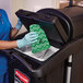A gloved hand using a green Rubbermaid microfiber cloth to clean a black cleaning cart.