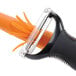A white OXO "Y" peeler with a julienne blade peeling a carrot.