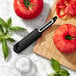 An OXO vegetable peeler next to a tomato and a knife on a cutting board.