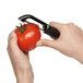 A person using an OXO straight serrated peeler to peel a tomato.