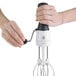 A hand holding an OXO Good Grips stainless steel manual egg beater with a black handle.