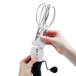 A hand holding an OXO Good Grips stainless steel and black manual egg beater with a white handle.