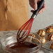 A person using an OXO Good Grips silicone whisk to stir chocolate liquid in a bowl.