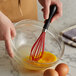 A hand using an OXO Good Grips silicone balloon whisk to mix eggs in a bowl.
