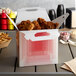 A red plaid barn take-out lunch box filled with fried chicken on a table.