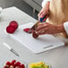 A person cutting a beet on a white Thunder Group cutting board with a knife.