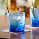Two Arcoroc blue rocks glasses with blue liquid and lime slices on a napkin.