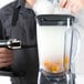A person holding a Breville smoking gun over a blender with liquid in it.