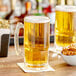 Two Acopa customizable beer mugs filled with beer on a table with a bowl of pretzels.
