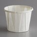 A white Genpak paper souffle cup with a white rim on a gray surface.