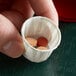A hand holding a Genpak paper souffle cup with pills inside.