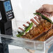 A hand using the Breville Sous Vide Circulator to cook ribs in a plastic bag with green herbs.