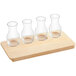 An Acopa natural wood flight tray holding empty 6 oz. glass carafes.