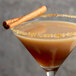 A glass of brown liquid with a DaVinci Gourmet Pumpkin Pie cocktail garnished with a cinnamon stick.