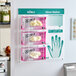 A wall-mounted glove dispenser station holding three boxes of Noble latex gloves with an attached usage guide chart.