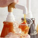 A hand pouring Torani Puremade Caramel Flavoring Sauce into a cup of ice.