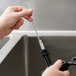 A person using a Carlisle white nylon spout brush with a wire to clean a faucet.