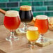 Four Acopa Belgian beer tasting glasses of beer on a table in a brewery tasting room.