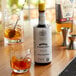 A bottle of Angostura Aromatic Bitters sits on a table with a glass of liquid and a cherry.