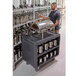 A man standing by a Cambro charcoal gray service cart with silver containers.
