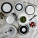 A table set with white and black Arcoroc plates and bowls with a white Arcoroc serving bowl filled with green leaves.
