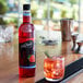 A bottle of DaVinci Gourmet sugar free strawberry syrup next to a glass of red liquid with ice.