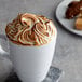 A white mug of coffee with brown and white foamy whipped cream on top.
