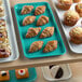 A green Cambro market tray of pastries and muffins on a bakery display counter.