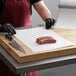 A person in black gloves cutting up sausages on a Choice white butcher paper-covered cutting board.