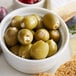 A white bowl filled with Belosa blue cheese stuffed green olives on a table with cheese and crackers.