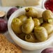 A bowl of Belosa sweet pickle stuffed queen olives on a table with other food.