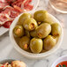A bowl of Belosa cheddar cheese stuffed green olives on a table with other food.