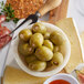 A bowl of green olives and cheese on a table.