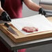 A person in a black apron cutting Choice white butcher paper on a cutting board.
