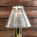 A Sterno table lamp with a clear glass pleated shade on a gold pole.