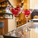 A pair of Chef & Sommelier wine glasses with red liquid and cherries on a bar counter.