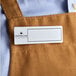 A white rectangular Cawley nametag on a brown apron.