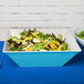 A salad in a blue GET Seabreeze square melamine bowl on a table.