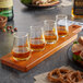 An Acopa Dual-Sided Flight Paddle holding four whiskey tasting glasses filled with amber liquid on a table.