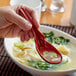 A person holding a red Thunder Group wonton soup spoon over a bowl of soup.